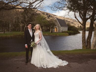 A bride and groom stand by the lake with Gougane Barra Church behind them | Wedding Photographer Cork