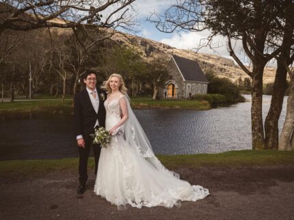 A bride and groom stand by the lake with Gougane Barra Church behind them | Wedding Photographer Cork