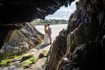 A bride and groom stand in the entrance to a cave on Inchydoney beach in West Cork