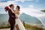 A groom and bride with blowing veil embrace on the headland overlooking the sea at Inchydoney Lodge and Spa