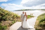A bride and groom stand facing the camera with Inchydoney beach behing=d them