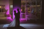 A bride and groom are silhouetted in pink light outside bridesmaid in creative light at Inchydoney Lodge and Spa