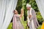 An Indian bride and groom in traditional wedding clothes laugh during the garland ceremony