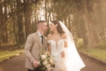 A newly married couple laugh together in a wooded garden