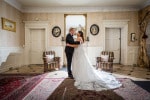 A newly married couple stand backlit in an ornate room
