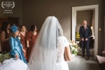 A brides father sees her for the first time in her wedding dress as her mother and the bridesmaids look on